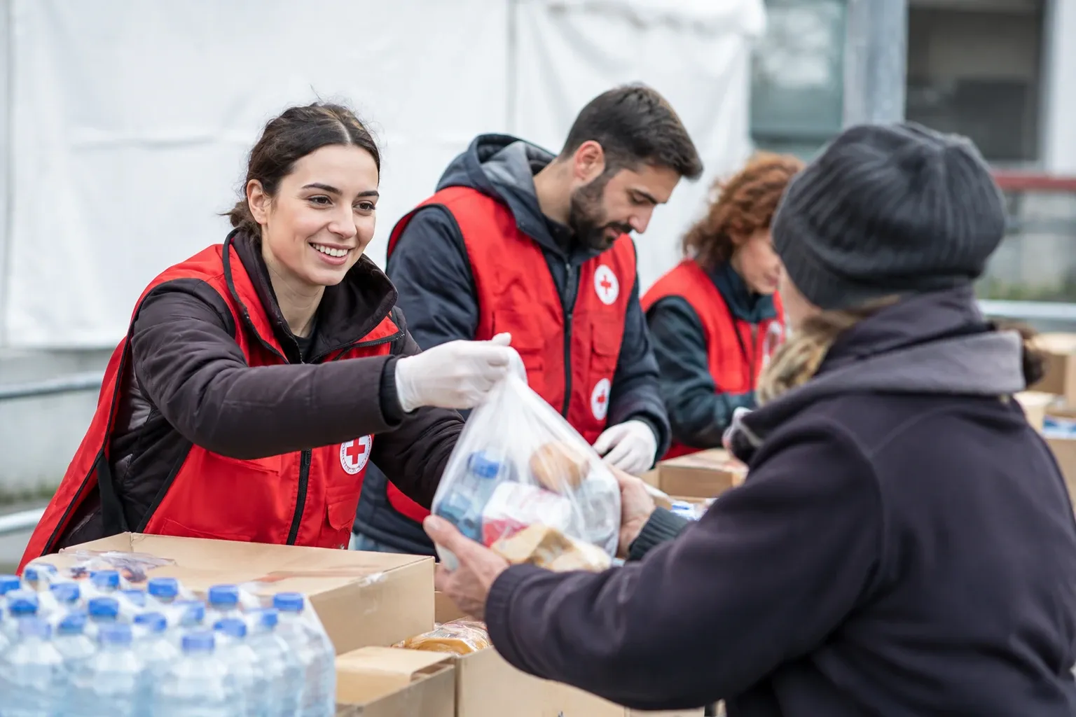 Volontaria sorridente distribuisce borsa di viveri a persona davanti al bancone outdoors