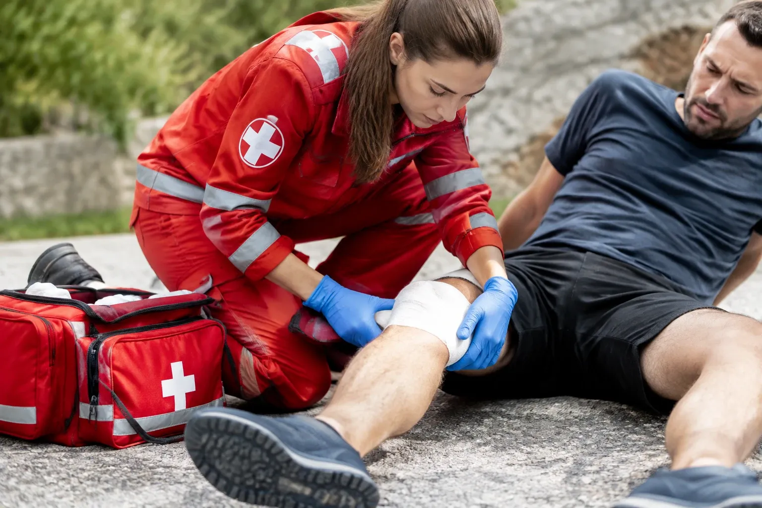 Soccorritrice in divisa applica bendaggio al ginocchio di un uomo seduto