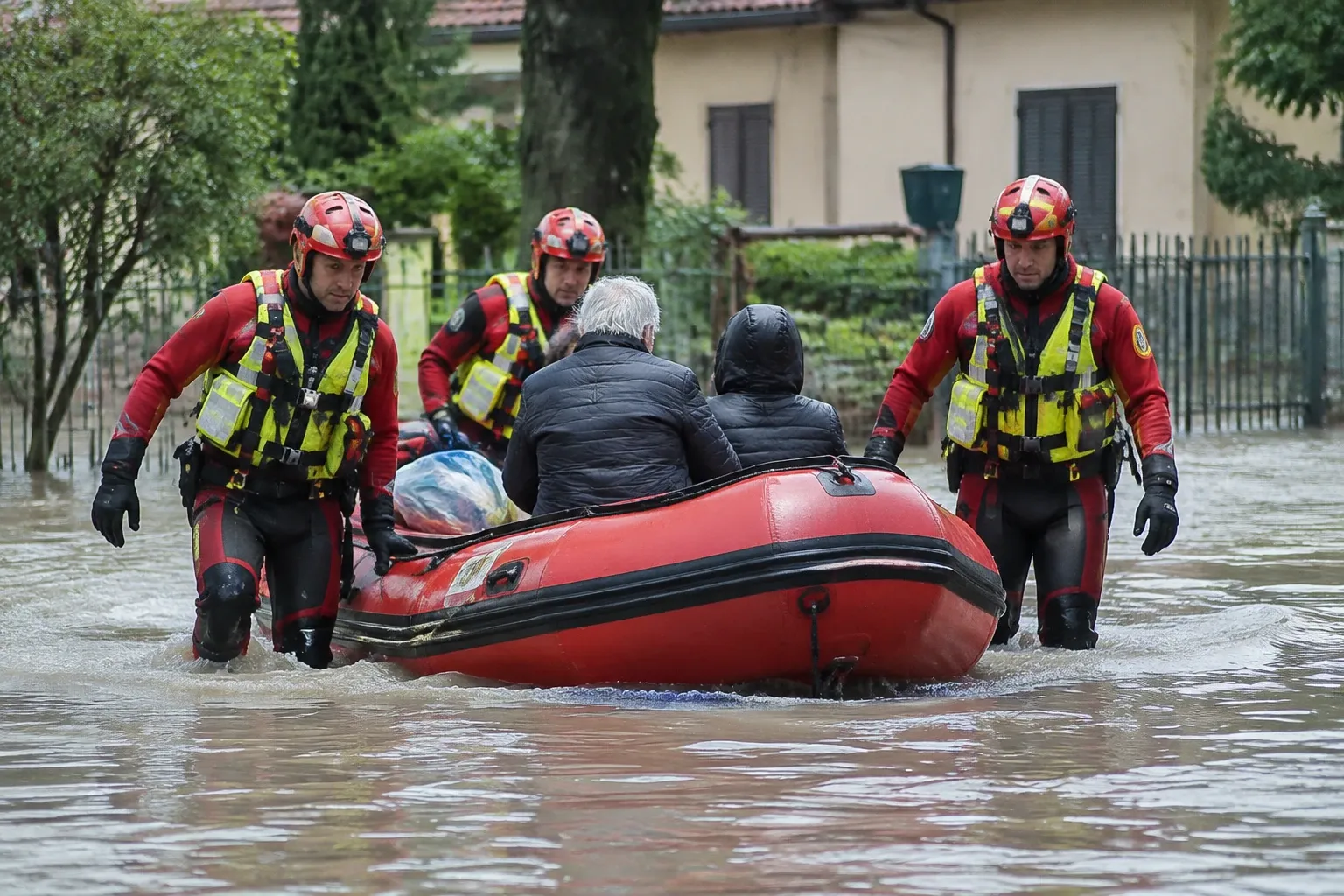 Volontari protezione civile con casco spingono gommone rosso con due evacuati nella piena