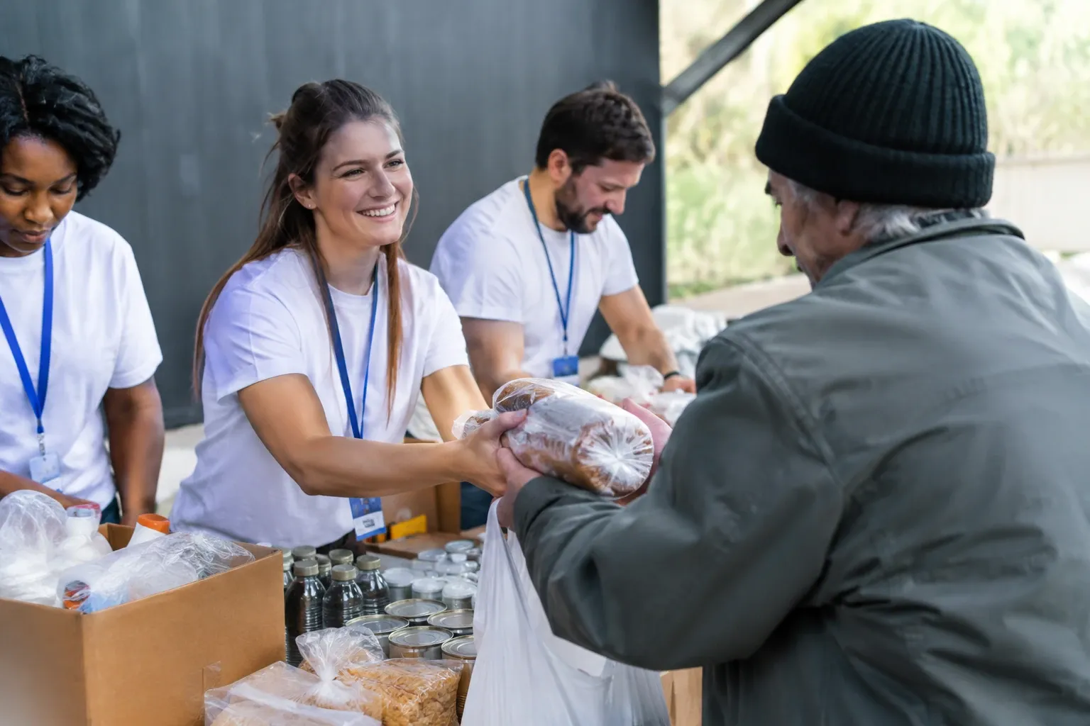 Volontaria sorridente che porge pane confezionato a uomo anziano durante distribuzione alimentare